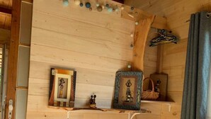 A wooden cabin room with a bed, two framed pictures on a shelf, and a hanging light fixture. - Chalet du Moulin des Fontaines (Saint-Paul-les-Fonts)