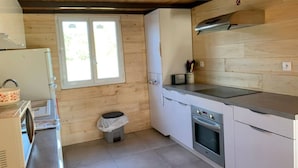 A compact kitchen with wooden walls, a window, a sink, a stove, and cabinets. - Chalet du Moulin des Fontaines (Saint-Paul-les-Fonts)
