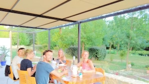 A covered outdoor dining area with a table and chairs, surrounded by greenery and trees. - Chalet du Moulin des Fontaines (Saint-Paul-les-Fonts)