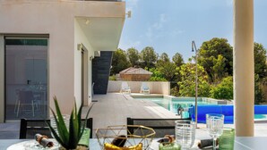A modern outdoor dining area with a pool, chairs, and a view of the surrounding greenery. - Villa Sophia (Busot)