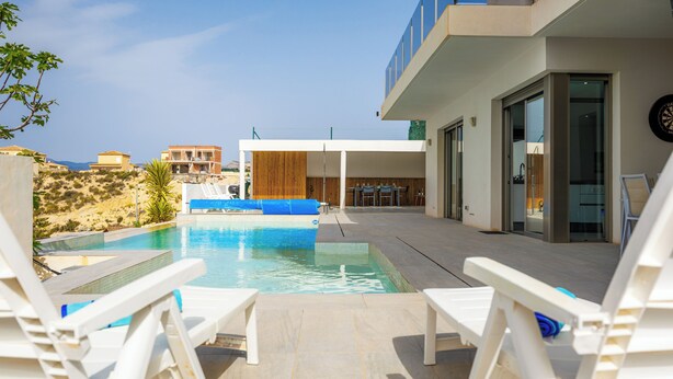 A modern pool area with white lounge chairs, a clear sky, and a view of the surrounding landscape. - Villa Sophia (Busot)