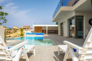 A modern pool area with white lounge chairs, a clear sky, and a view of the surrounding landscape. - Villa Sophia (Busot)
