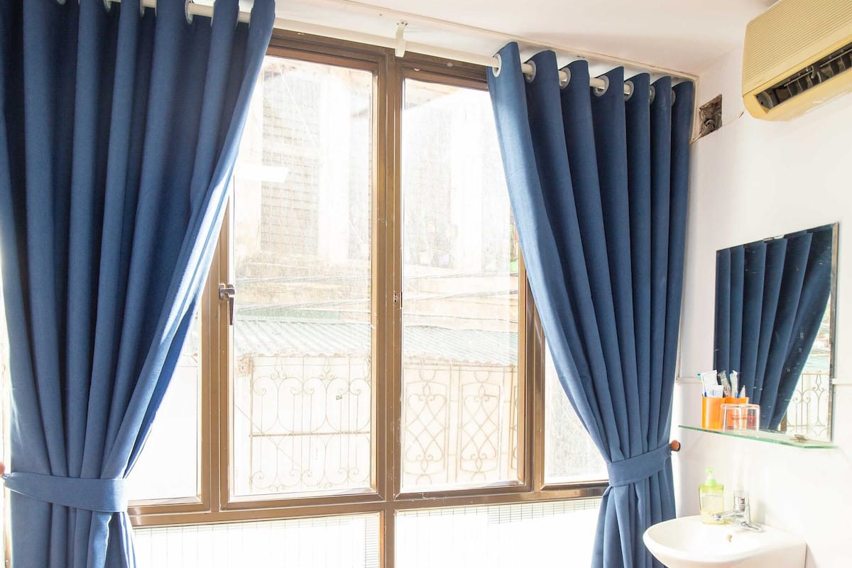 A room with a bed, a window with curtains, a sink, and a mirror.
