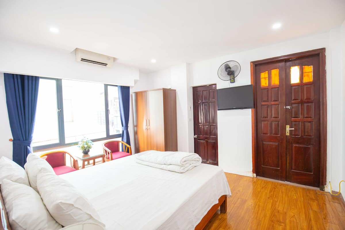 A hotel room with a bed, a desk, a chair, a wardrobe, and a door.