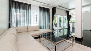 A modern living room with a beige sofa, a glass coffee table, and sheer curtains. - Perfect holiday home (Hua Hin)
