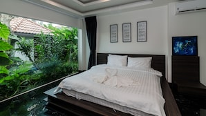 A modern hotel room with a large bed, a view of greenery through a glass wall, and motivational wall art. - Perfect holiday home (Hua Hin)