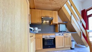 Eine Küche mit Holzausstattung, einem Bosch-Ofen, einer Kaffeemaschine und einem Fernseher auf einem Regal.