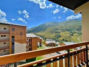 A modern building with wooden paneling and balconies, overlooking a valley with mountains and a clear sky. - Cozy apartment 50m from slopes, 2 rooms for 6 people, balcony and available services (Les Menuires)
