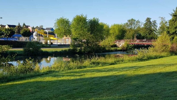 A park with a pond, a playground, and a bridge. - Camping La Sittelle (Loue)