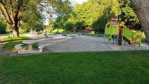 A playground with a slide and climbing structures, surrounded by trees and a picnic table. - Camping La Sittelle (Loue)
