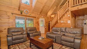 L’intérieur d’un chalet en bois comprend deux fauteuils inclinables en cuir, une table basse en bois et un escalier.