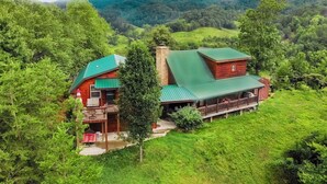 Une cabane dotée d’un toit végétalisé, d’une cheminée et d’un balcon donnant sur une vallée verdoyante.