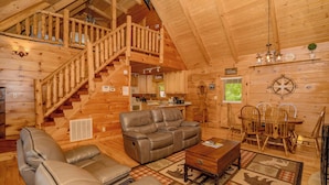L’intérieur d’une cabane en rondins, avec un escalier en bois, un canapé en cuir, une table à manger et des chaises.