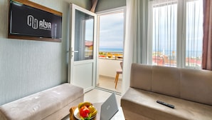 Een hotelkamer met balkon, een bank, een laptop en een televisie waarop de naam van het hotel staat.