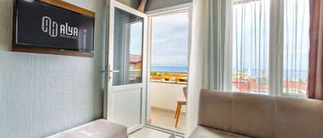 A hotel room with a balcony, a sofa, a laptop, and a TV displaying the hotel name.