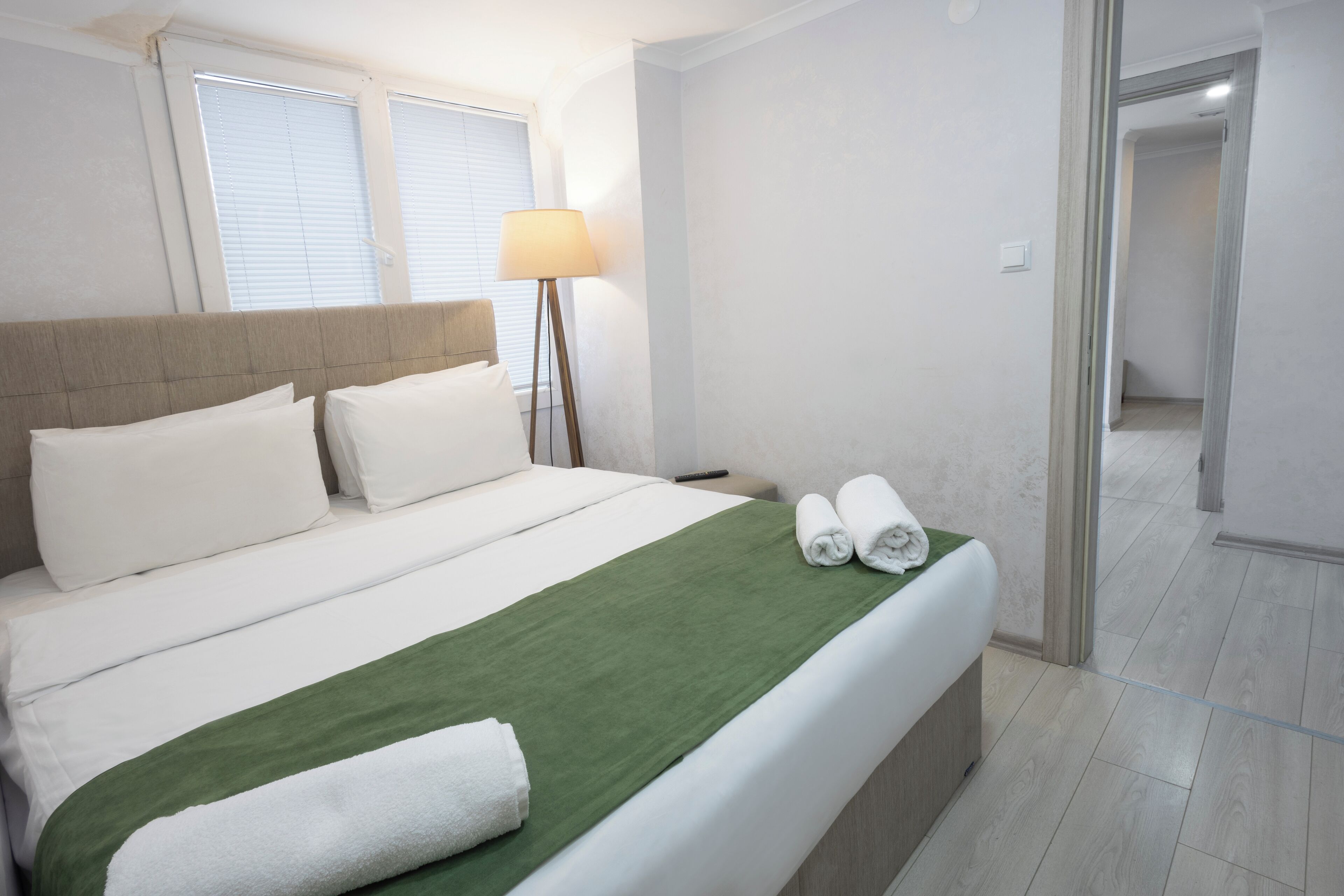A hotel room with a bed, a lamp, and a view of the hallway.