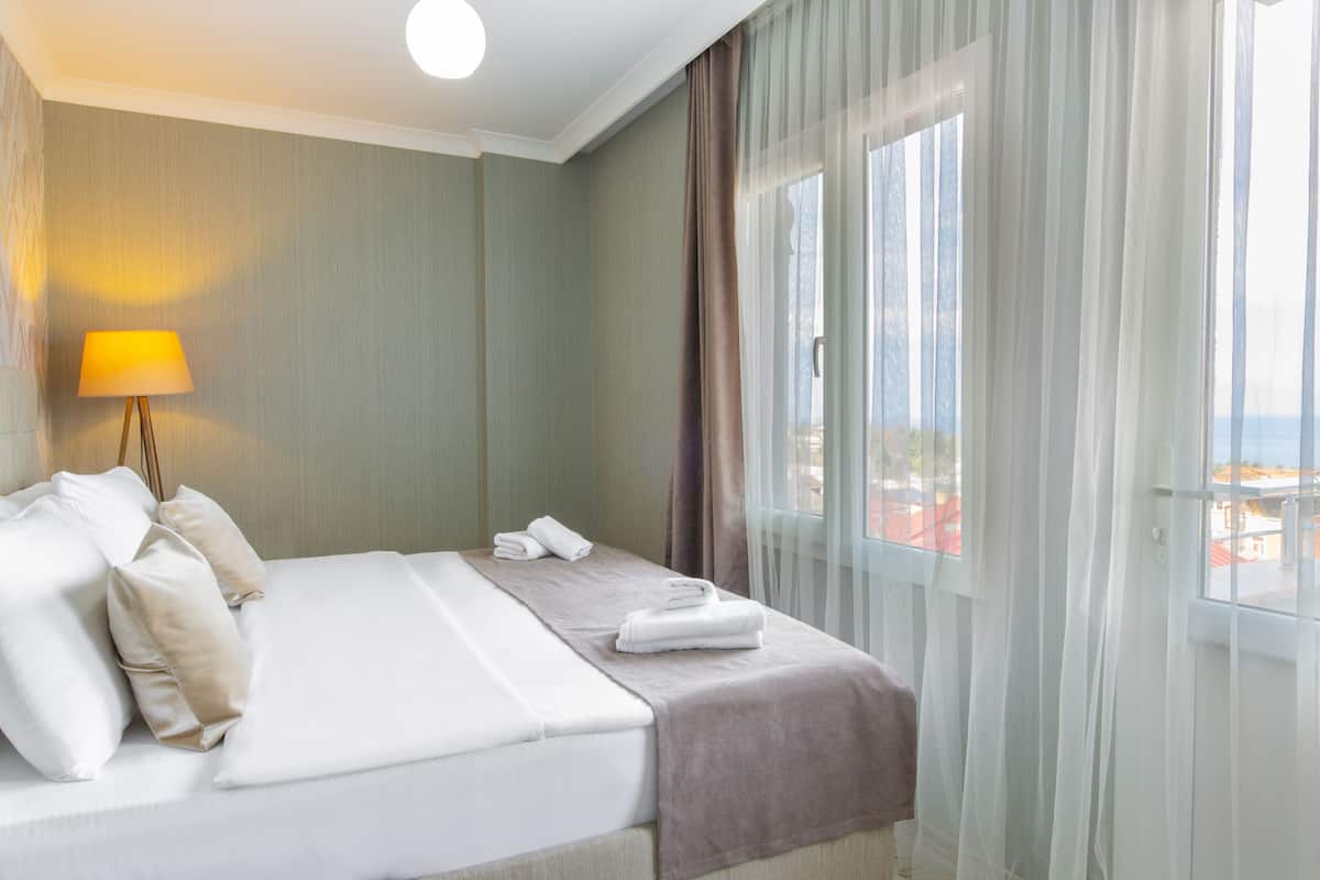 A hotel room with a bed, pillows, a lamp, a window with curtains, and a view of the outside.