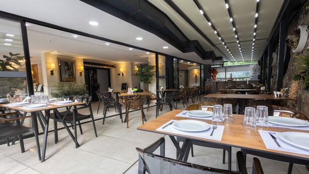 Een restaurant met meerdere tafels gedekt voor diners, met een modern interieur van houten tafels en zwarte stoelen.