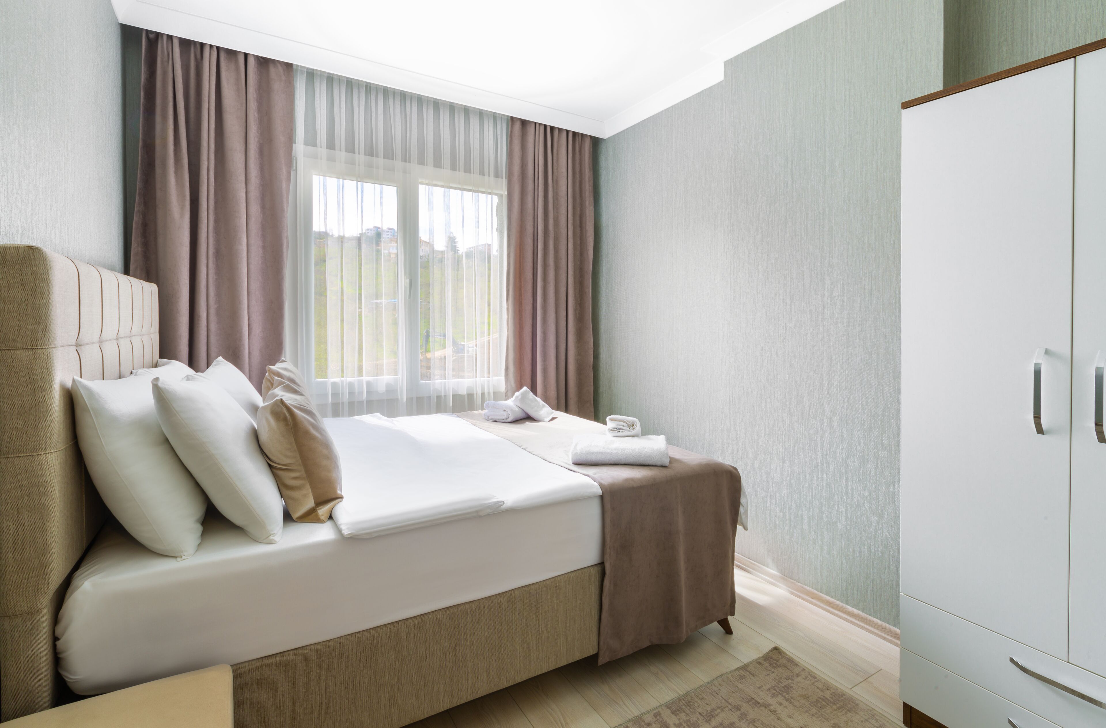Ein Hotelzimmer mit Bett, Nachttisch, Schrank und einem Fenster mit Vorhängen.