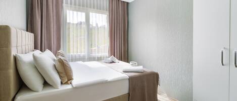 Ein Hotelzimmer mit Bett, Nachttisch, Schrank und einem Fenster mit Vorhängen.