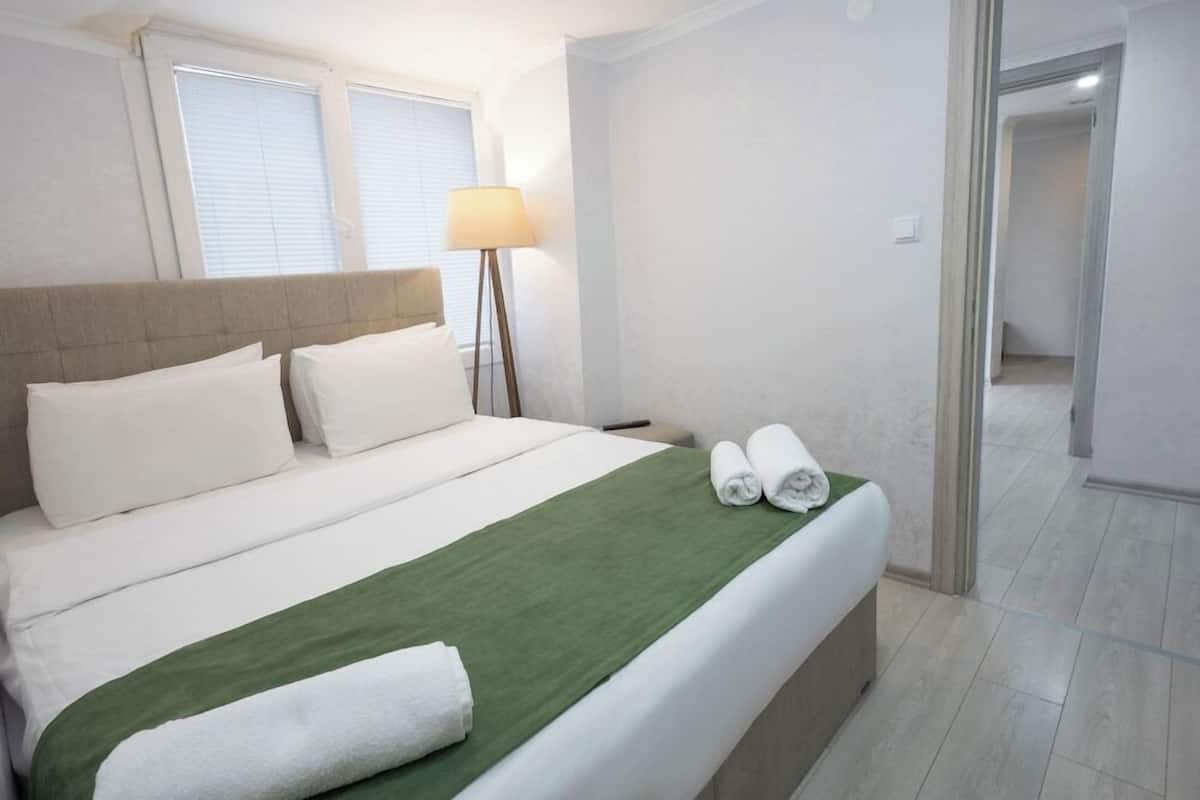 A hotel room with a bed, a lamp, and a view of a hallway.
