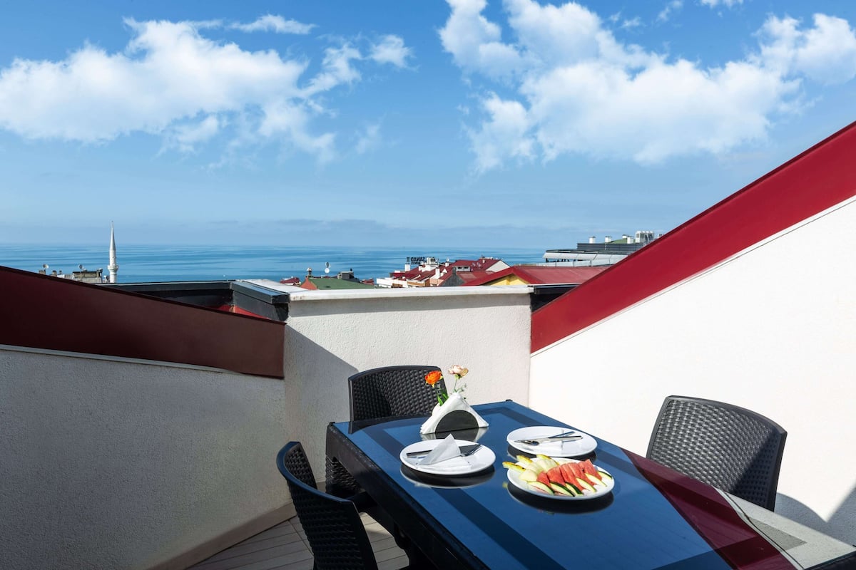 A dining table with plates of food and a view of the sea and buildings in the background.