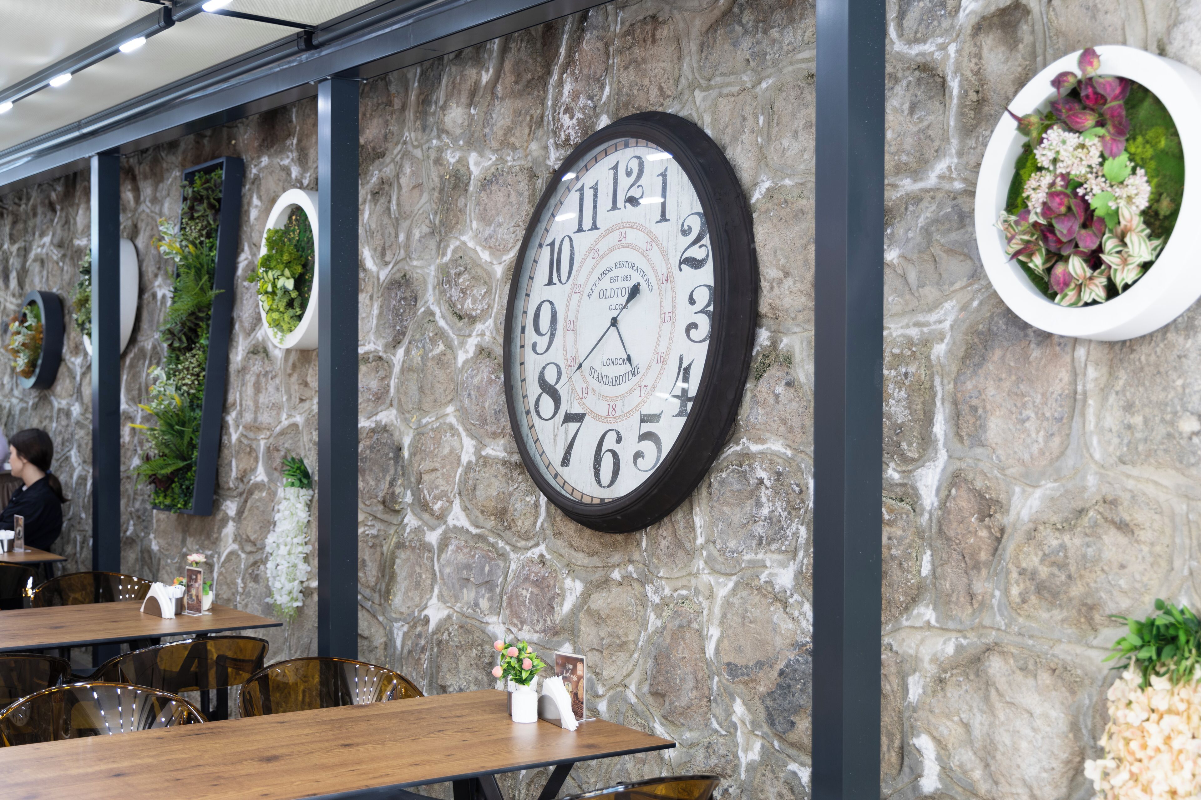 A restaurant interior with stone walls, a large clock, and several tables with chairs.