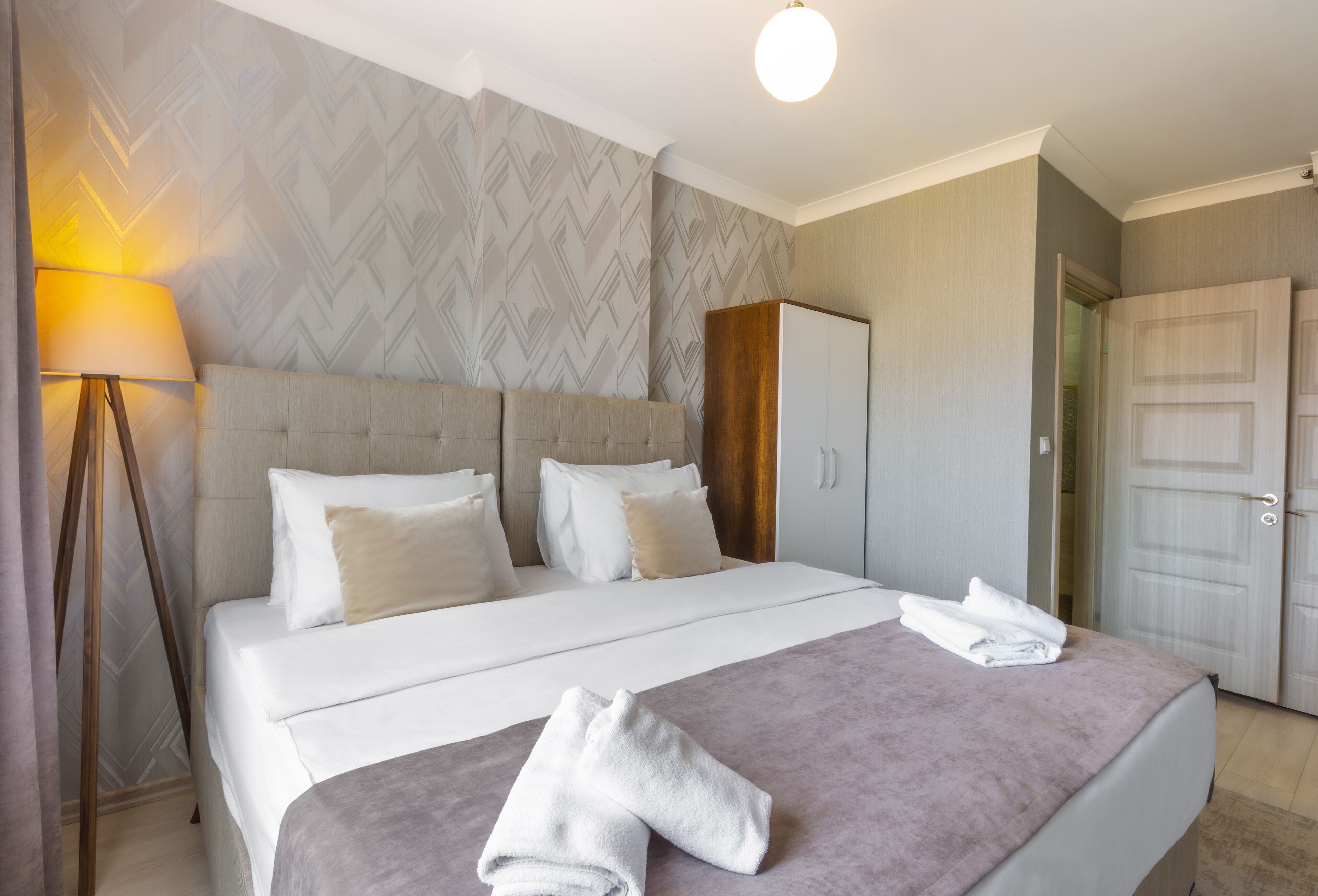 A hotel room with a large bed, a wardrobe, and a lamp.