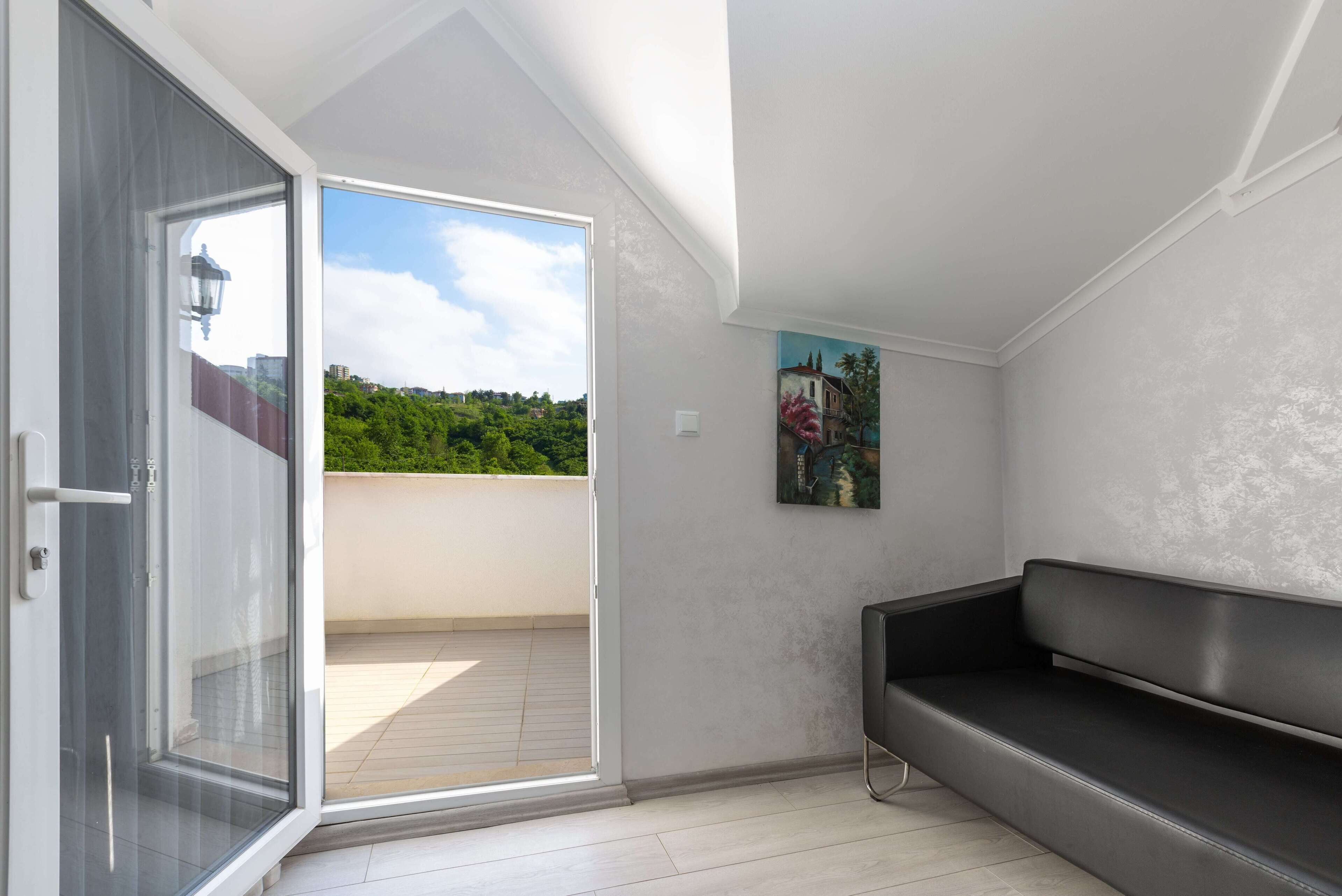 A modern room with a sliding glass door leading to a balcony, a black sofa, and a painting on the wall.