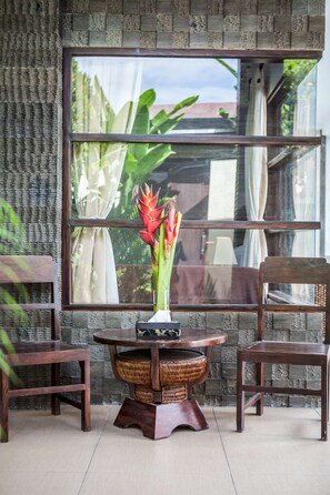Enjoy a peaceful retreat with a view of lush greenery from the large window, accompanied by a comfortable seating area with a wooden table and two chairs.