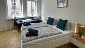 A modern bedroom with a large bed, two smaller beds, a window with a view, and a small bedside table with a plant. - Apartment in the heart of Bad Pyrmont (Bad Pyrmont)