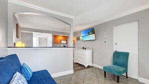Una sala de estar con un sofá azul, un sillón verde azulado y un televisor en la pared.