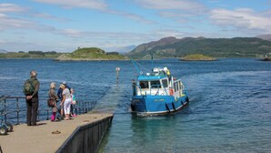 A boat named "The Lisheen" docked at a pier with people standing on the adjacent platform. - The Old Byre at Dallachulish. (Oban)