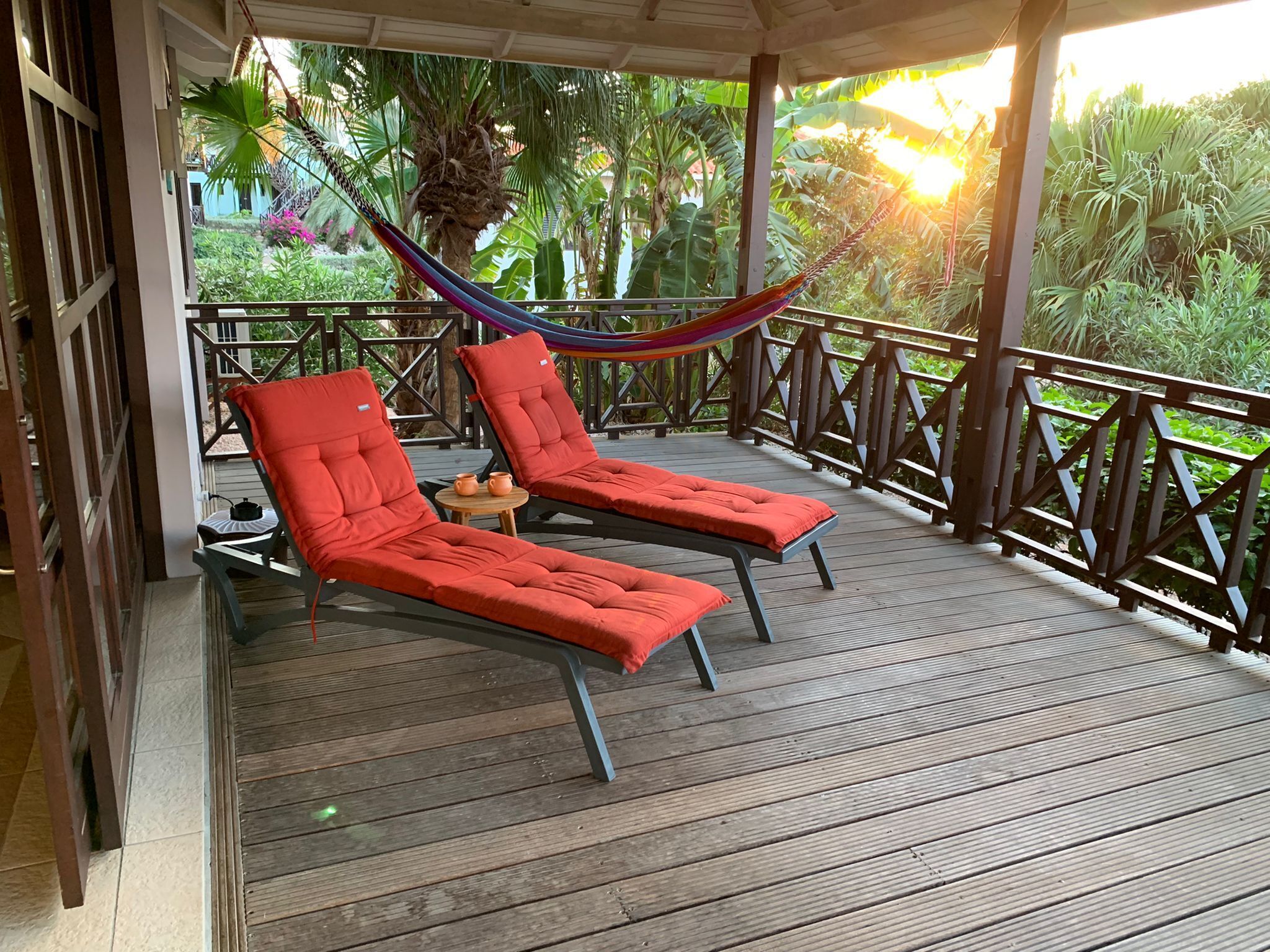 A wooden deck with two red lounge chairs and a hammock.