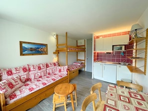 Um quarto de estudante com beliches, um sofá, uma mesa pequena e um kitchenette.