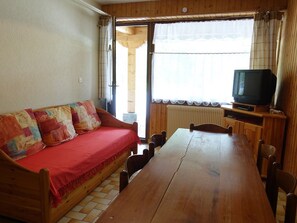 Um interior em madeira com um sofá, uma TV sobre um suporte e uma mesa de jantar.