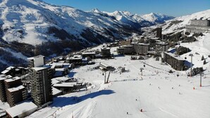 A snow-covered ski resort with multiple buildings, including hotels and possibly a ski lift area. - 2-room apartment, 6 pers., south-facing balcony, pets allowed (Les Menuires)