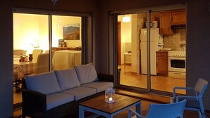 Un espace extérieur aménagé avec un canapé, des fauteuils et une table, donnant sur la cuisine et la salle à manger.