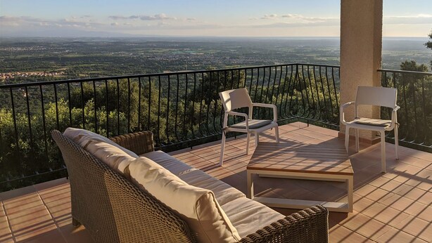 Un balcon agrémenté de meubles et de chaises en osier, offrant une vue sur un paysage lointain.