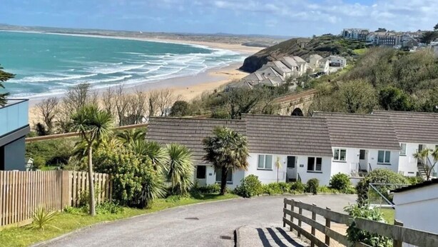 A coastal residential area with houses, a beach, and a clear sky. - Sea view apartment with balcony and gardens. Private path to the beach. (St Ives)