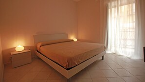 A bedroom with a bed, bedside tables, and a window with sheer curtains. - Terrazza Cathedral by Wonderful Italy (Cefalù)