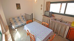 A compact kitchen with a dining table, chairs, a small television, and a window with curtains. - Terrazza Cathedral by Wonderful Italy (Cefalù)