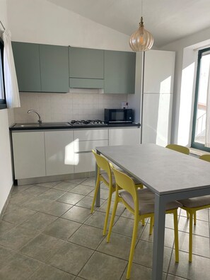 A modern kitchen with a dining area, featuring a gas stove, a microwave, and a hanging light fixture. - Terrazza Cathedral by Wonderful Italy (Cefalù)