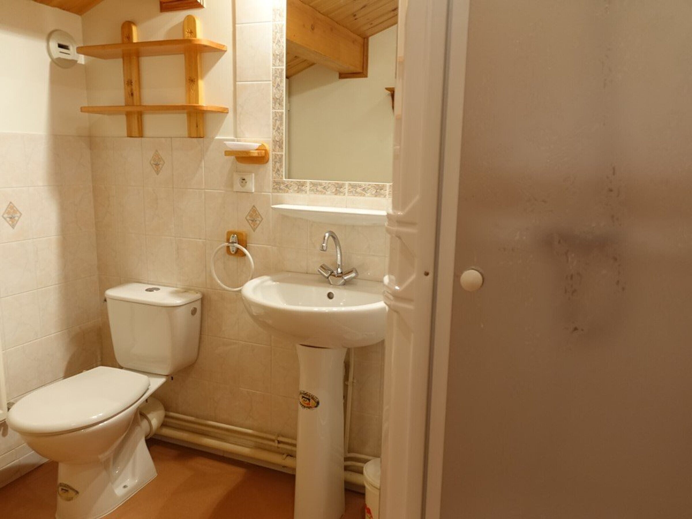 A bathroom with a toilet, sink, and wooden shelves.