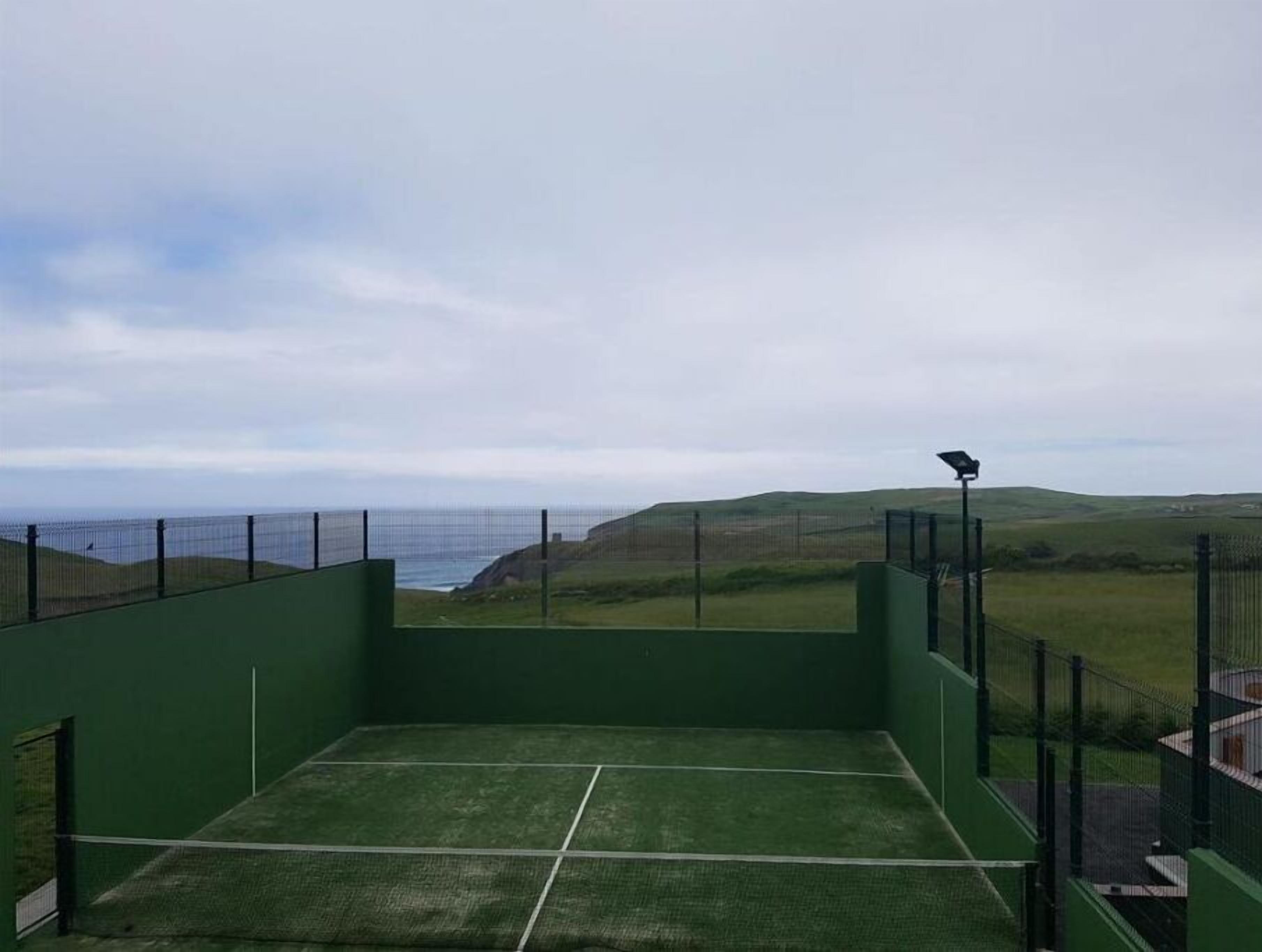 A tennis court with a view of the sea and hills.