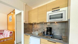 Cocina compacta con armarios de madera, microondas integrado, cafetera y lavavajillas.