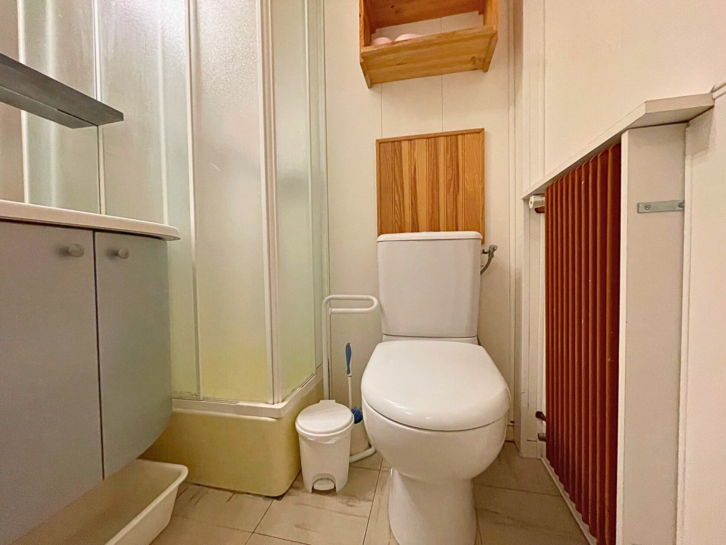 A compact bathroom with a toilet, a shower, and a small shelf above the toilet.