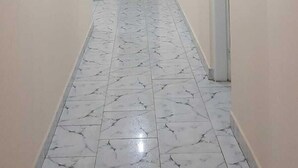 A hallway with a marble floor, white walls, a dark door at the end, and recessed ceiling lights.