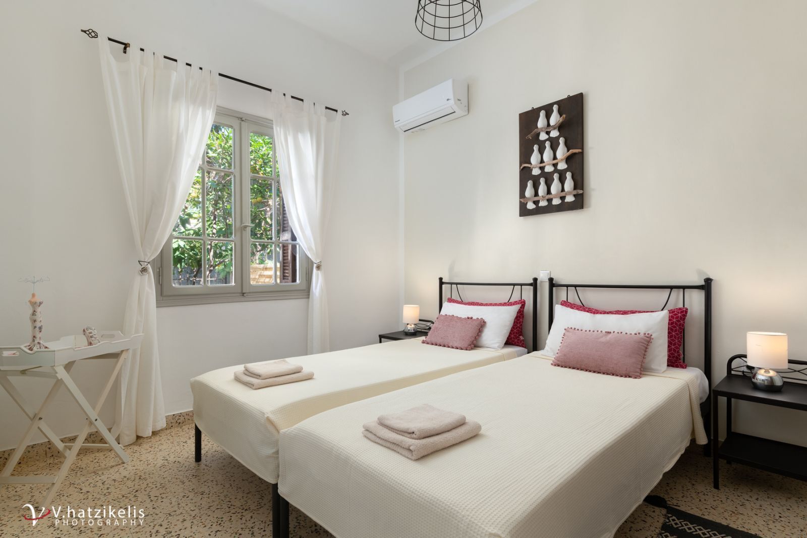 A double bed with two pillows, a bedside table, a lamp, and a window with curtains.