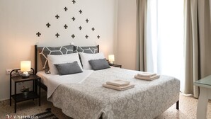 A neatly made bed with a geometric headboard, two bedside tables with lamps, and a decorative wall with fleur-de-lis patterns. - Aramis Boutique House, Medieval Old-Town Rhodes (Rodos)